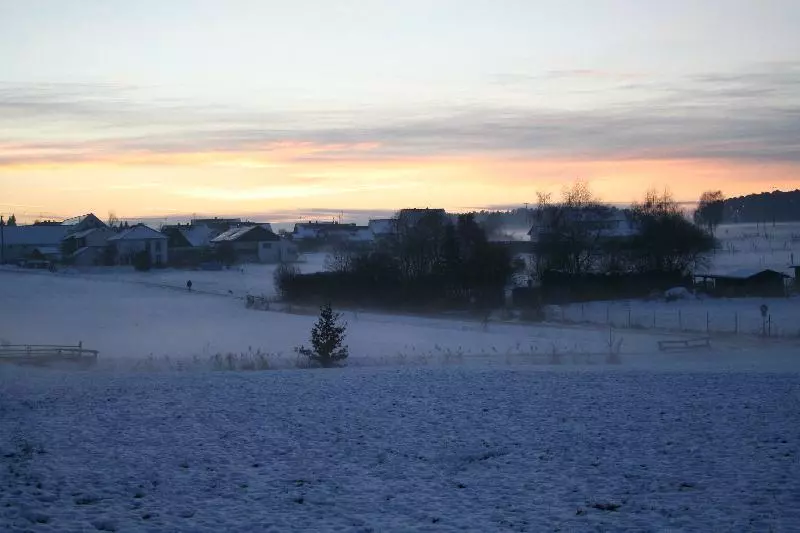 Verschneite Winterlandschaft mit Feld und Gebäuden (Symbolbild)